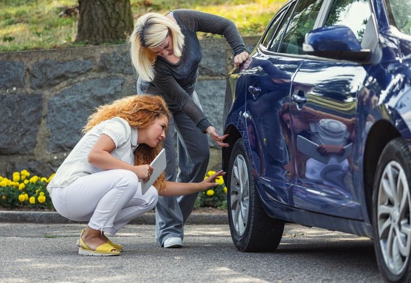 Two women inspect a car tire, emphasizing auto insurance services in the Grand Junction area.